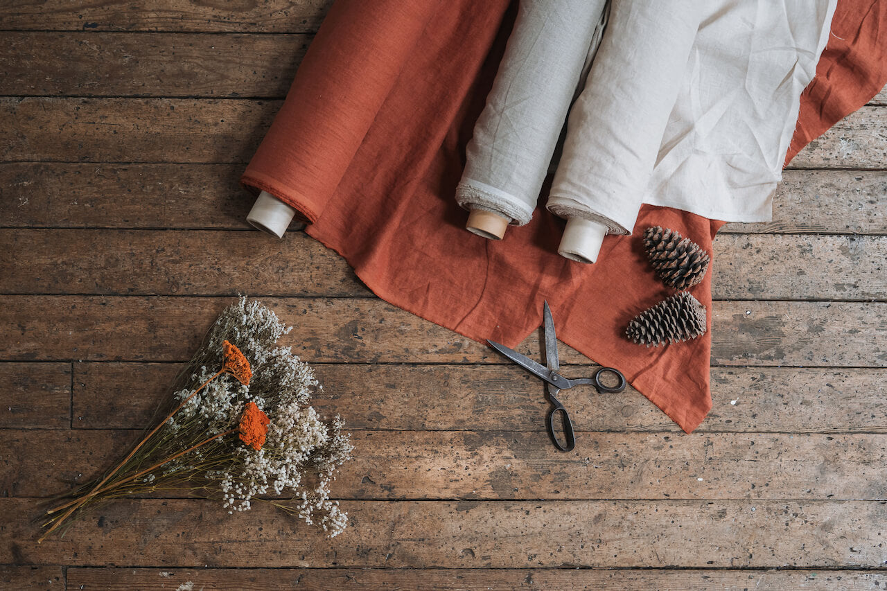 Terracotta and natural linen fabric rolls on wooden floor with dried flowers