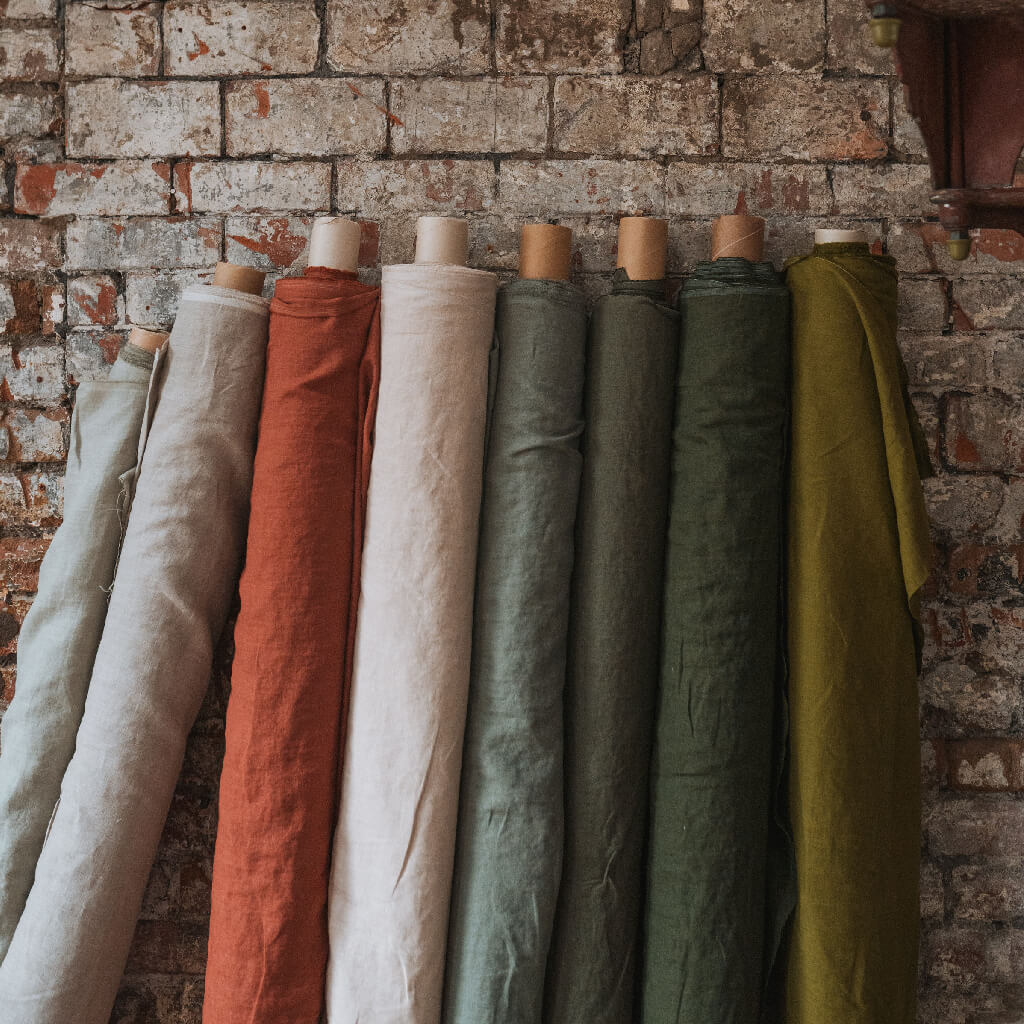 Linen fabric by the metre in stacked rolls against brick wall