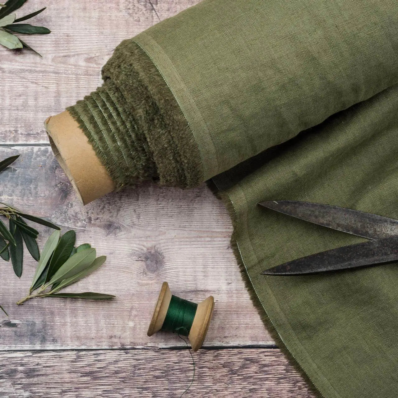 Olive Green linen fabric, ready to cut, with scissors, thread bobbins and plant leaves
