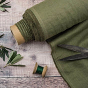 Olive Green linen fabric, ready to cut, with scissors, thread bobbins and plant leaves