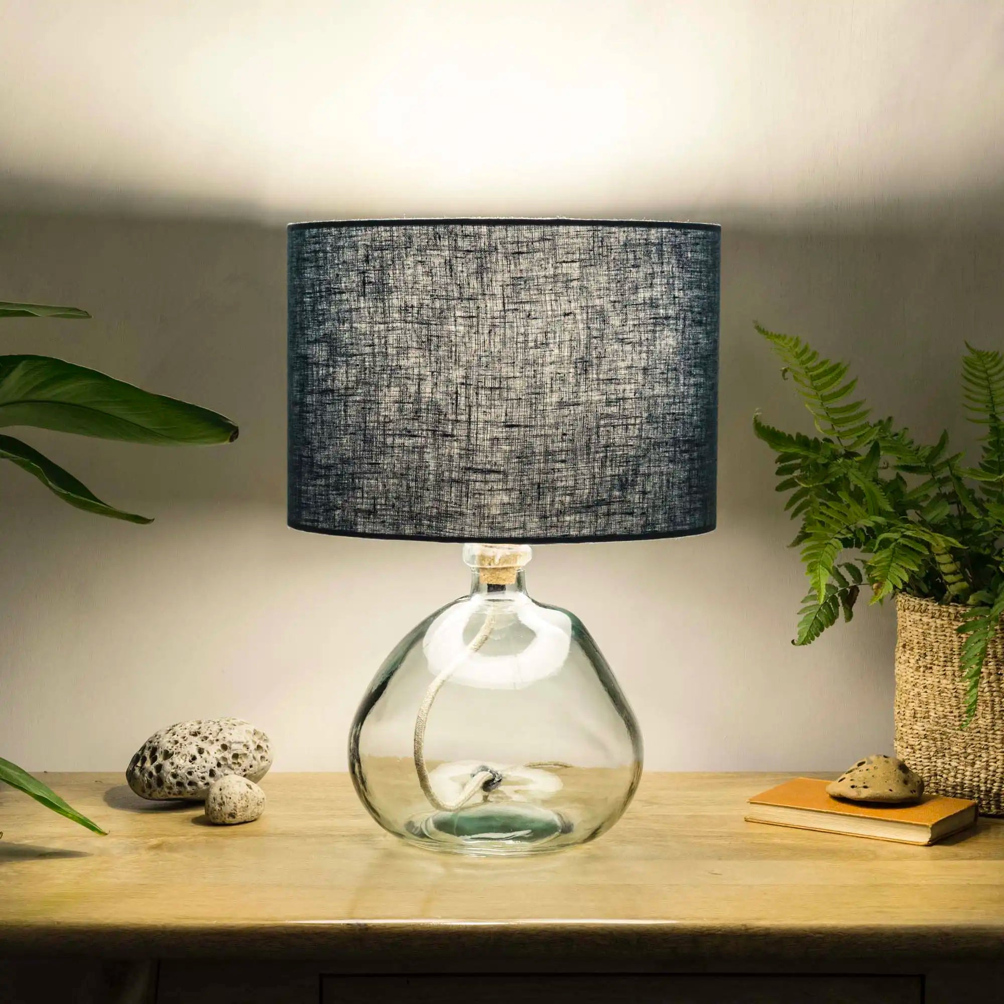 Dusty blue lampshade made from textured linen illuminated on recycled glass table lamp