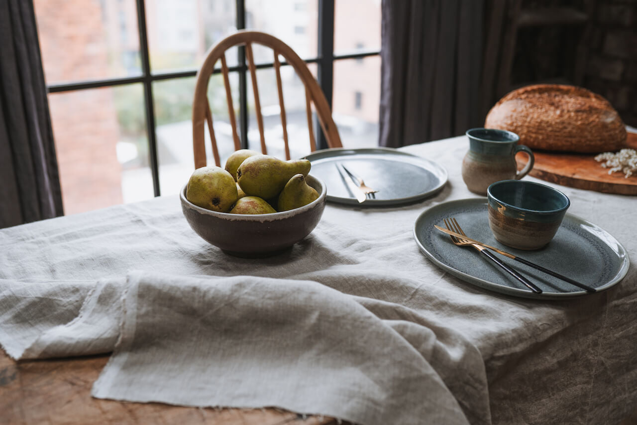 Linen table cloth with bowl of pears, plates and sourdough bread