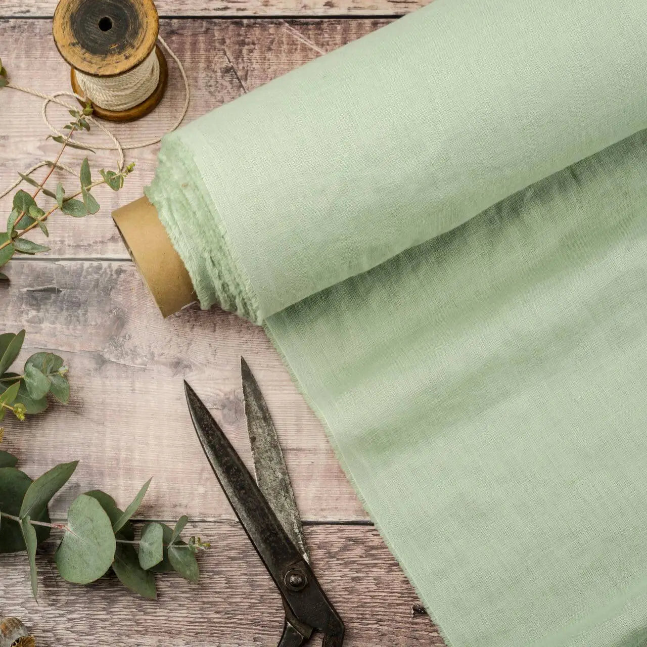 Pistachio Green linen fabric, ready to cut, with scissors, thread bobbins and eucalyptus 