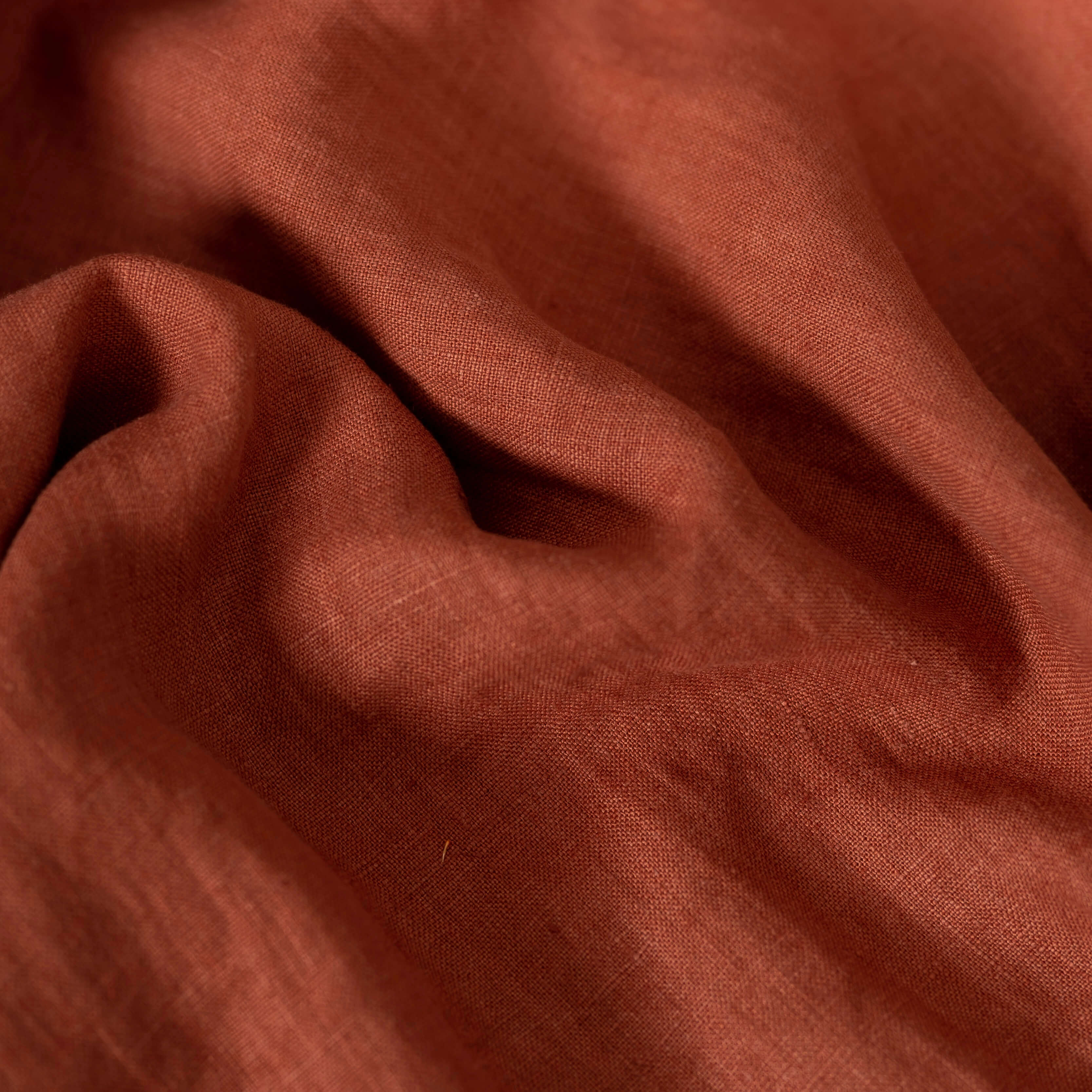 Terracotta linen fabric, folded to show its soft, natural texture