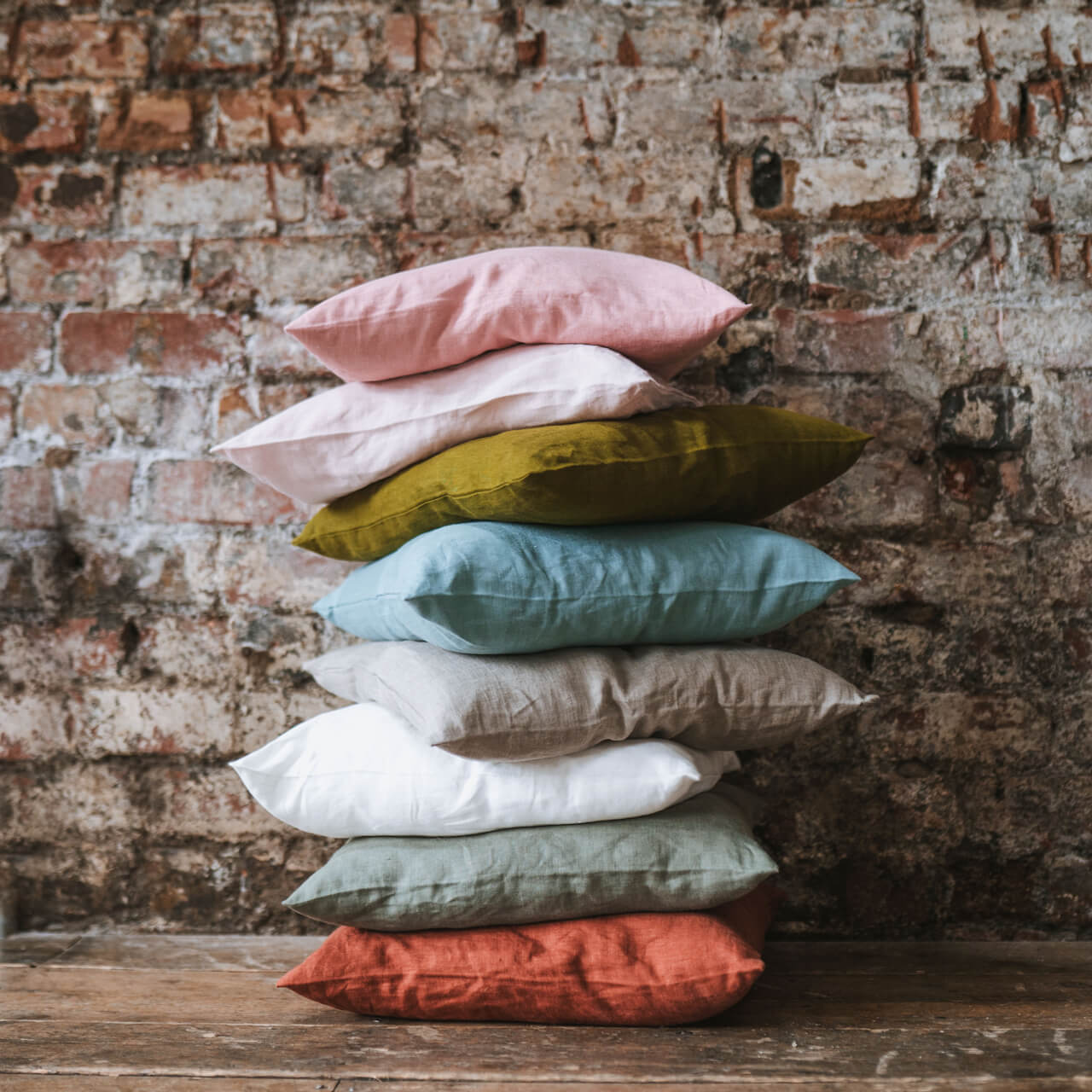 Linen cushions piled up on wooden floor agains brick wall