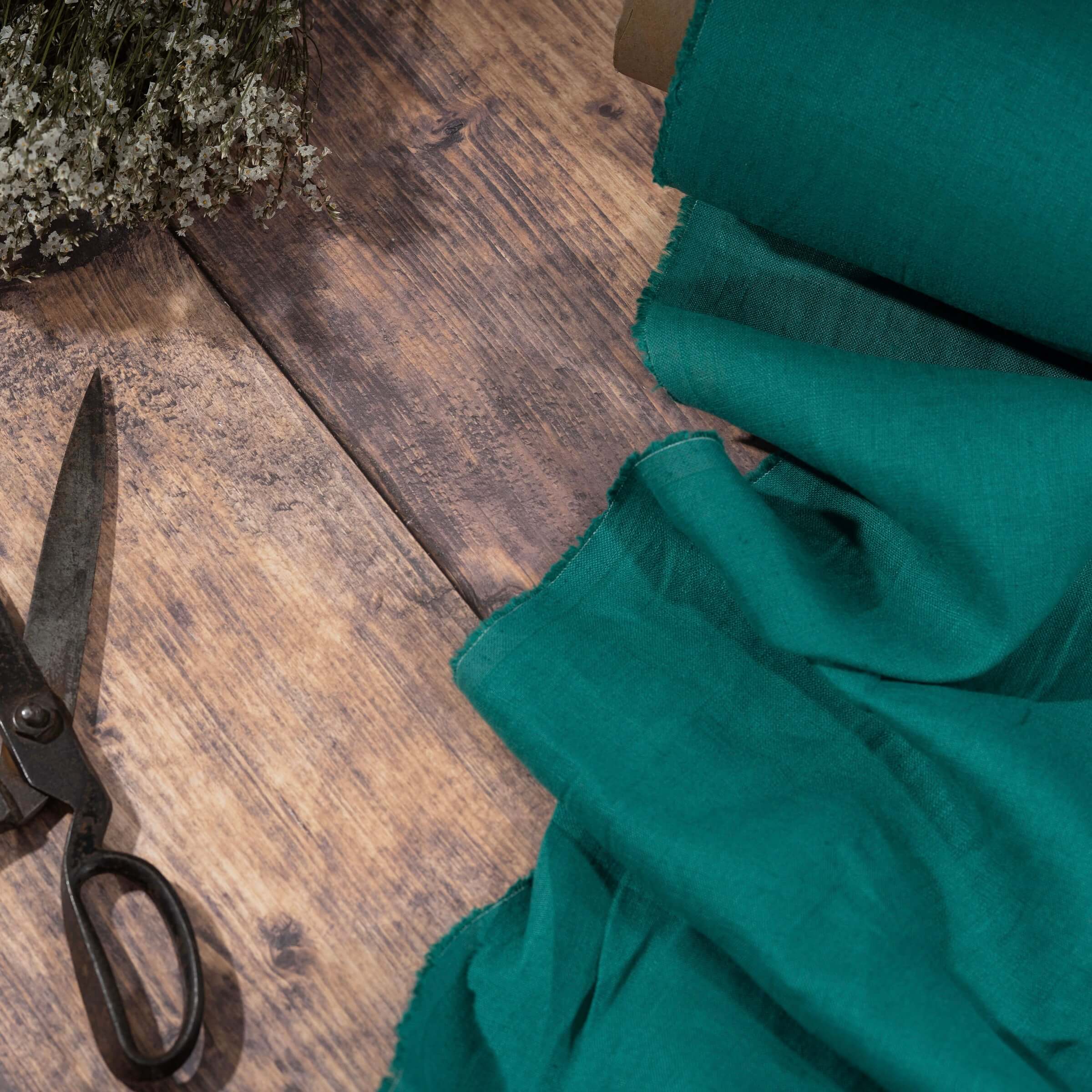 Emerald Green linen fabric on wooden table, ready to cut, with scissors and flowers