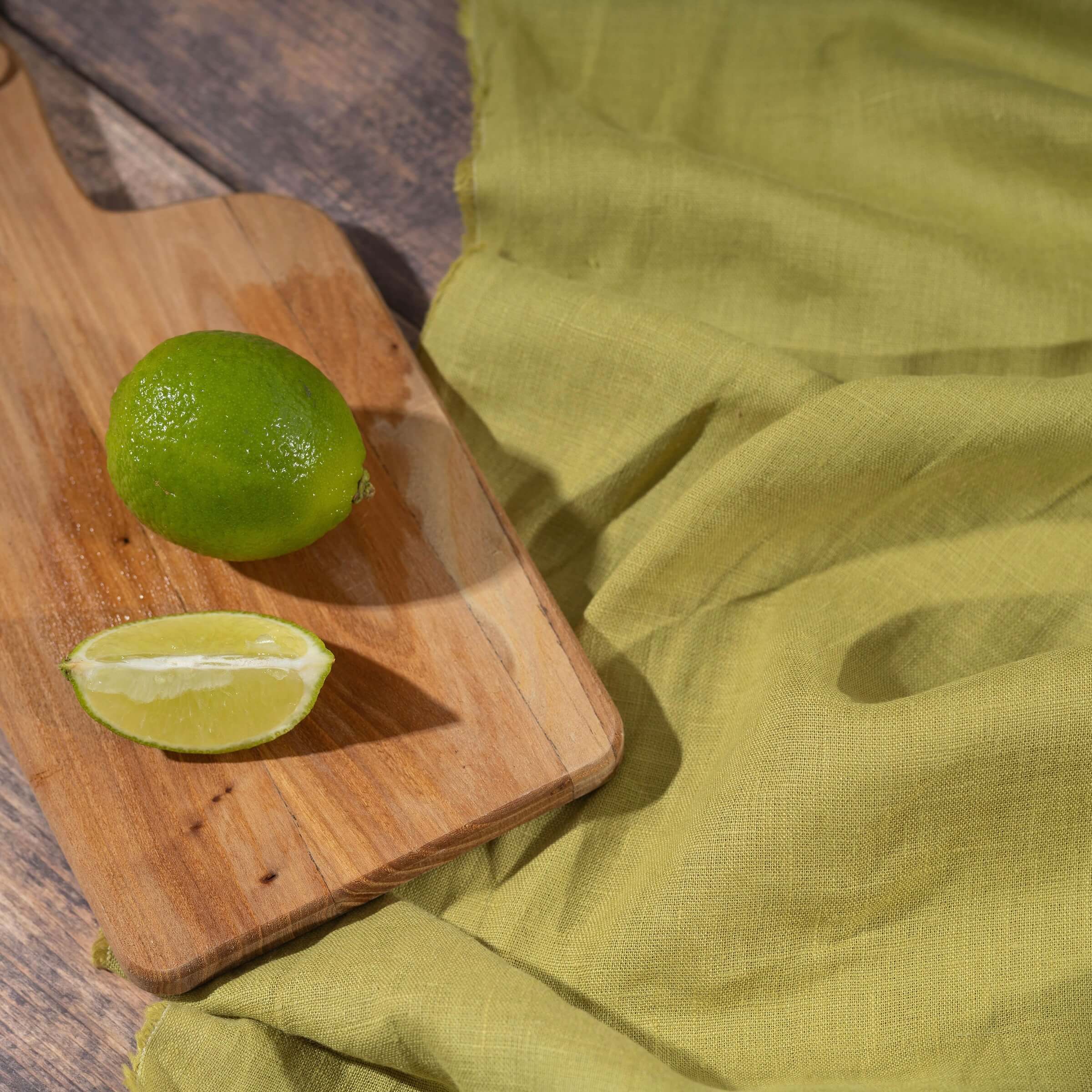 Lime Green linen fabric on wooden table, ready to cut, with limes on chopping board