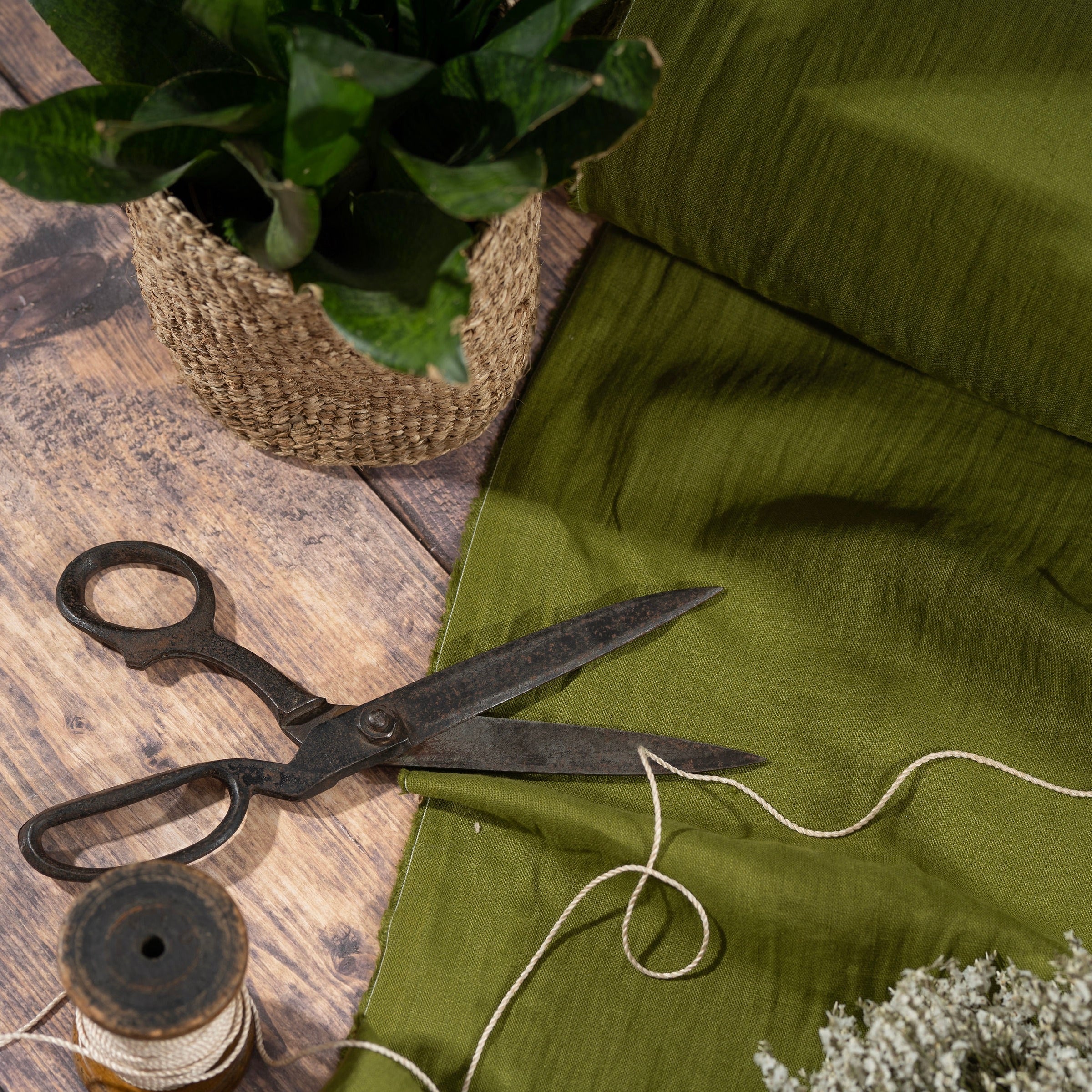 Moss Green linen fabric, ready to cut, with scissors, thread bobbins and plant in woven basket