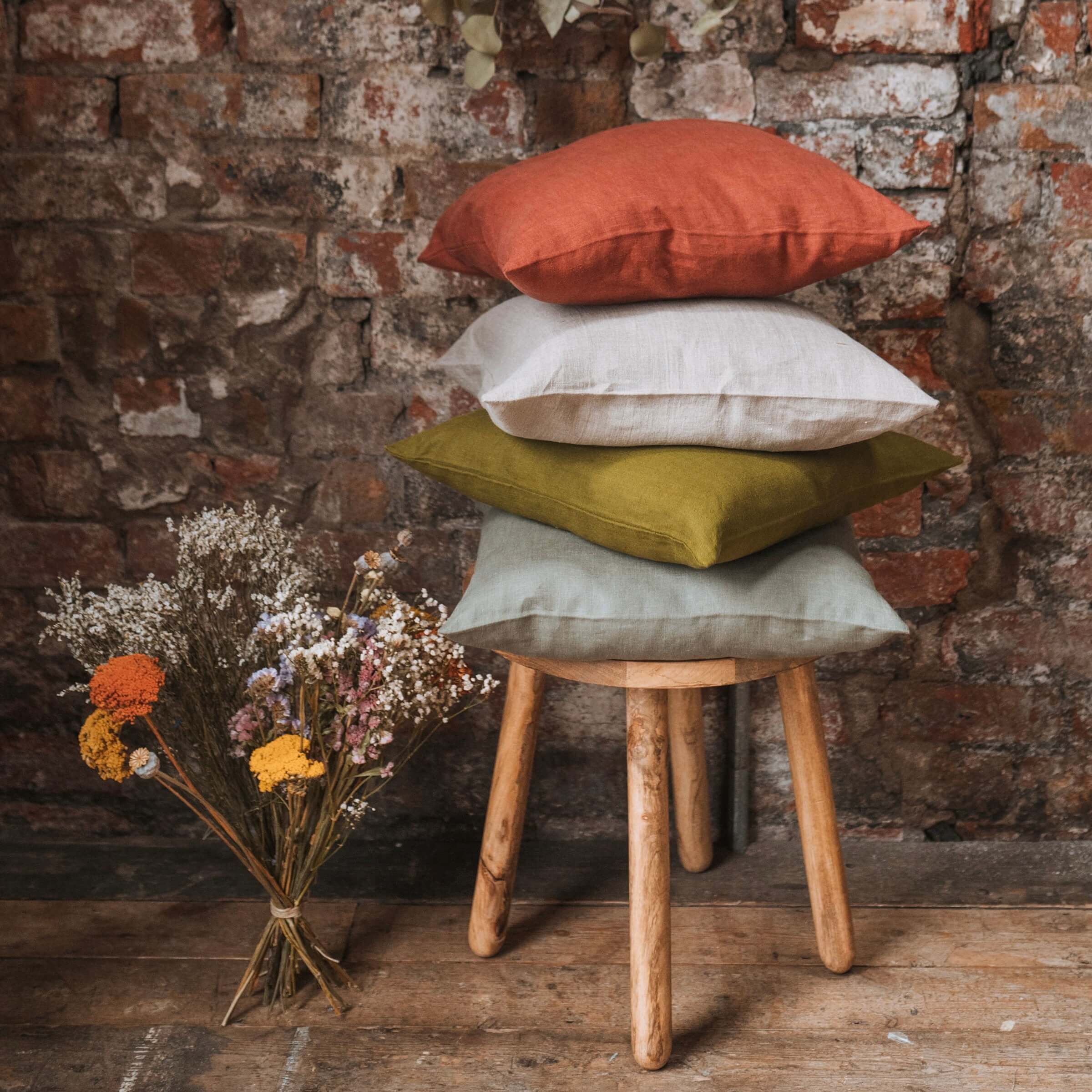 Stack of washed linen cushion covers on wooden stool with dried flowers