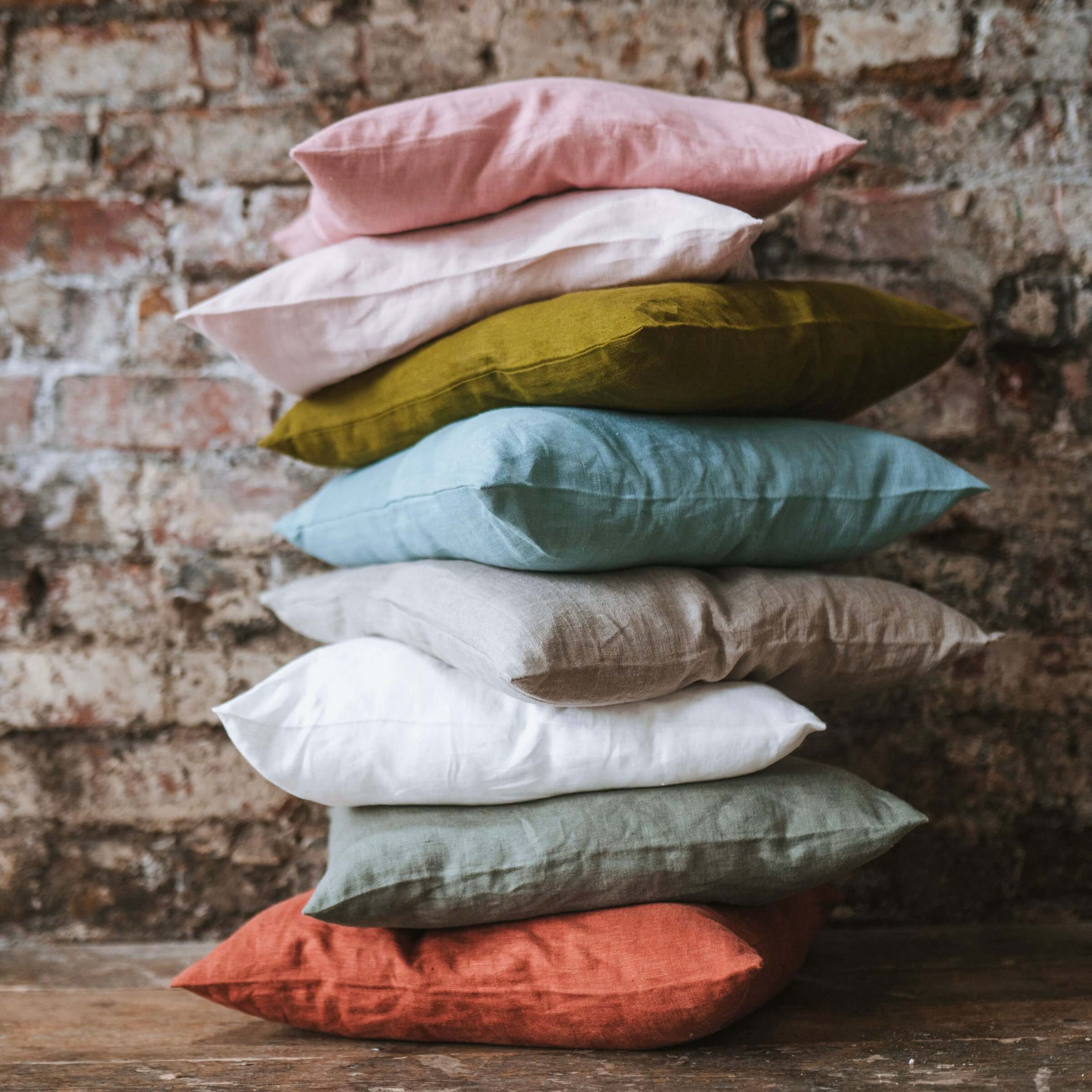 Collection of colourful linen cushion covers against exposed brick wall and on wooden floor