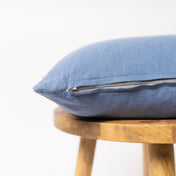 Dusty blue linen cushion cover with zipper closure on wooden stool