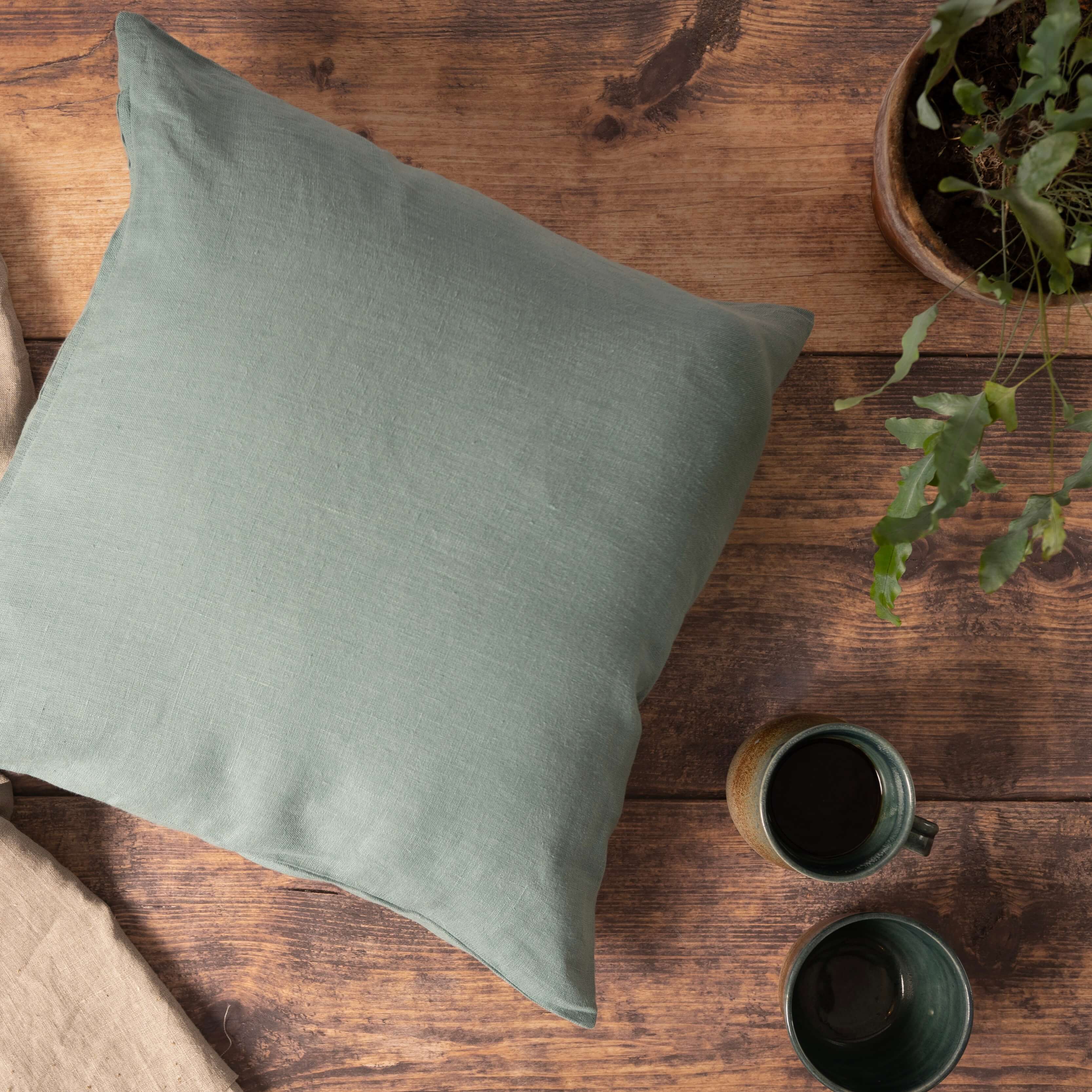 Dusty turquoise linen cushion cover on wooden table with cup of coffee and house plant