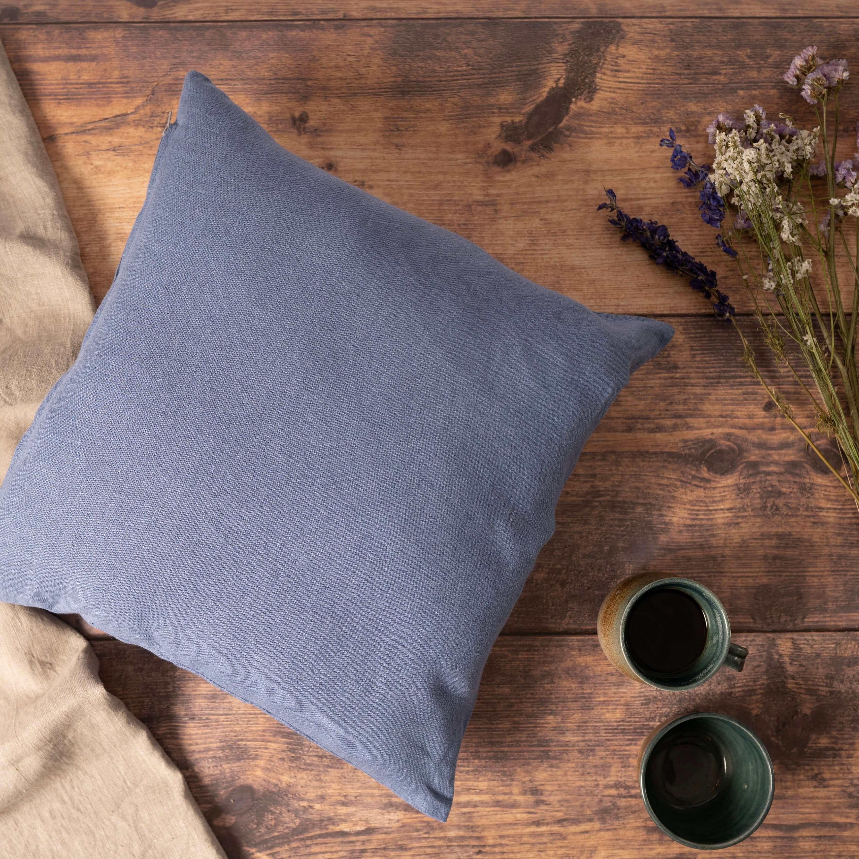 Dusty blue linen cushion cover on wooden table with coffee and wild flowers