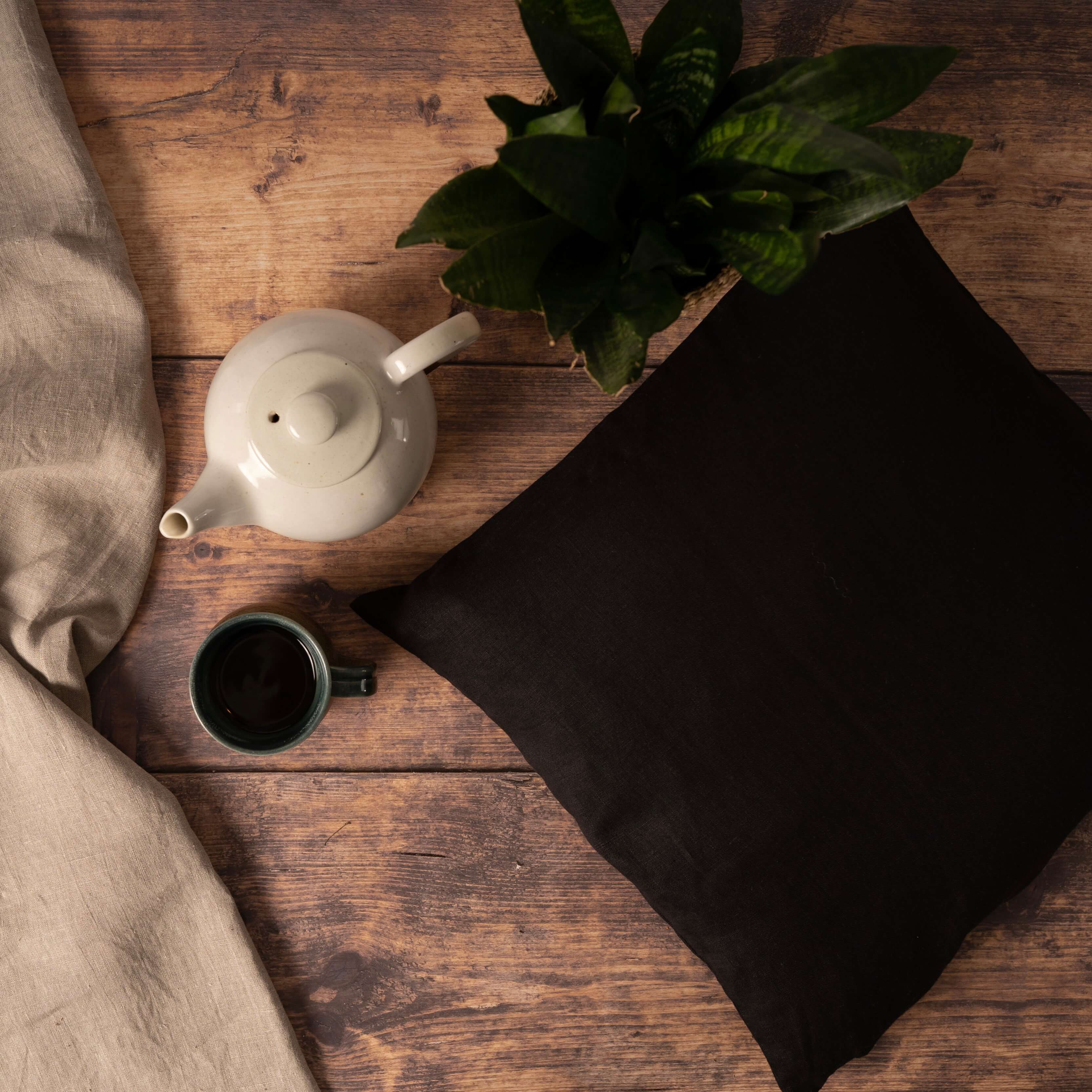 Black linen cushion cover on wooden table with plant and cup of coffee
