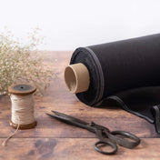 Roll of black linen fabric on wooden table with scissors and bobbin