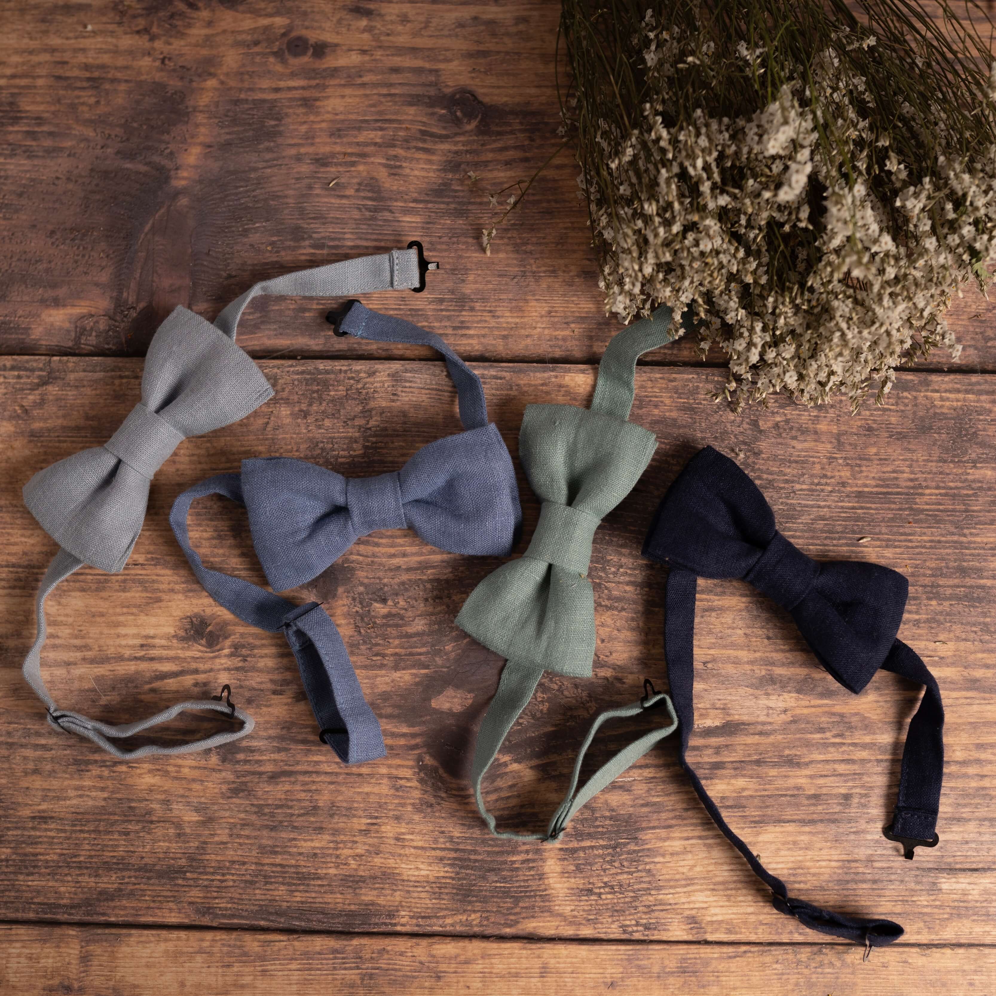 Collection of blue linen bow ties on wooden table with wild flowers