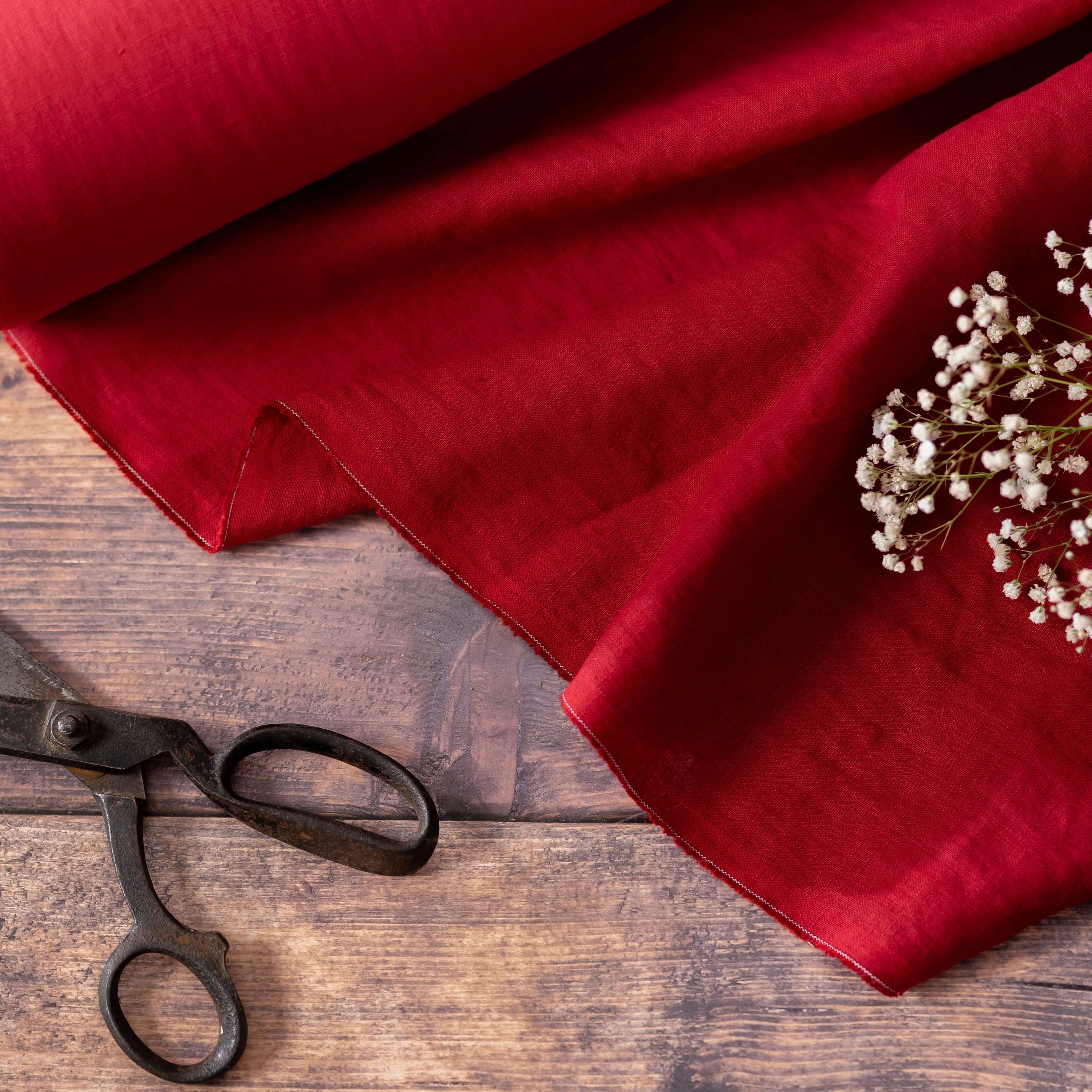 Berry red linen fabric on wooden table with wild flowers and scissors