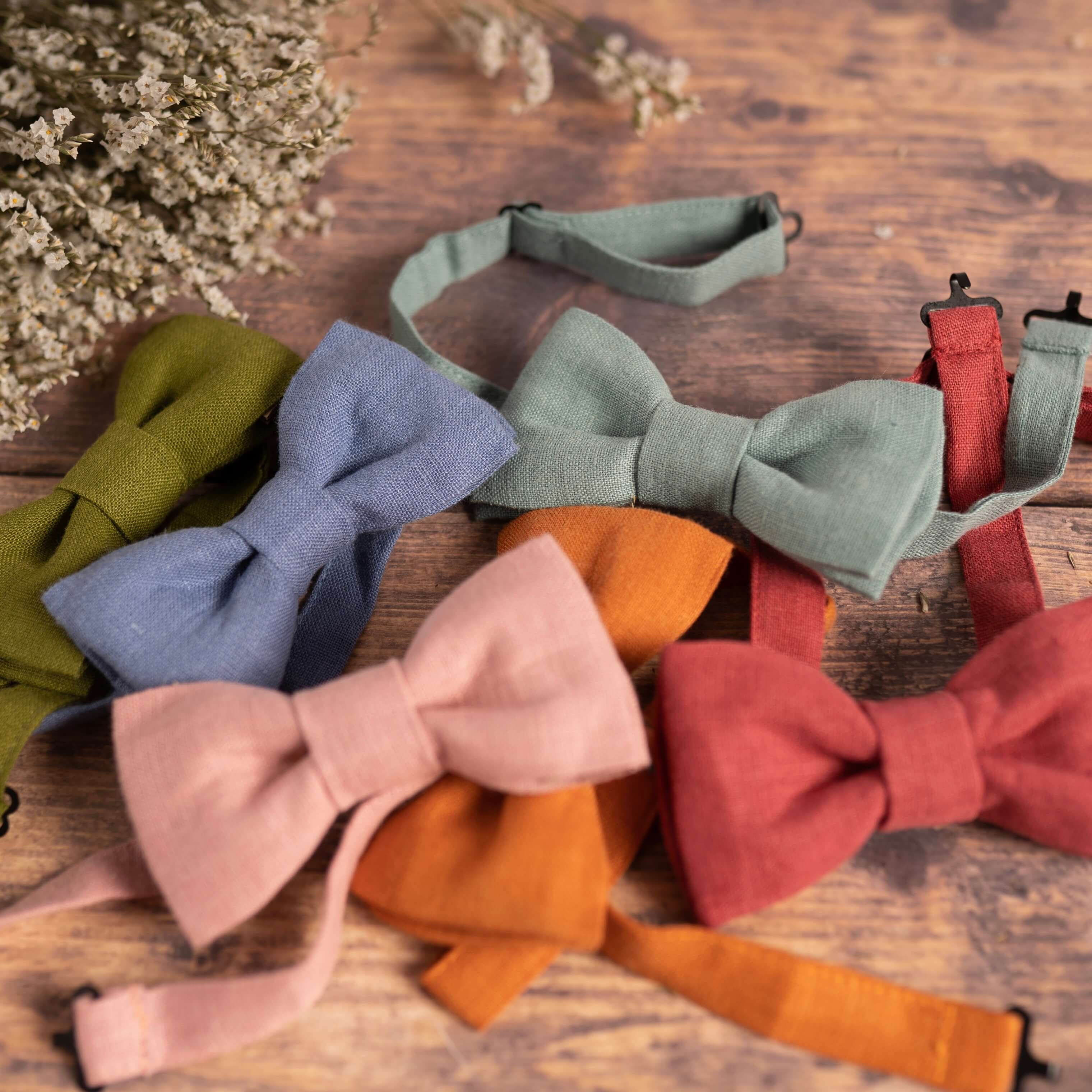 Selection of colourful linen bow ties on wooden table with dried flowers