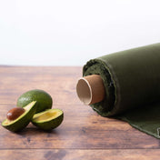 Avocado green linen fabric on roll with cut avocados on wooden table